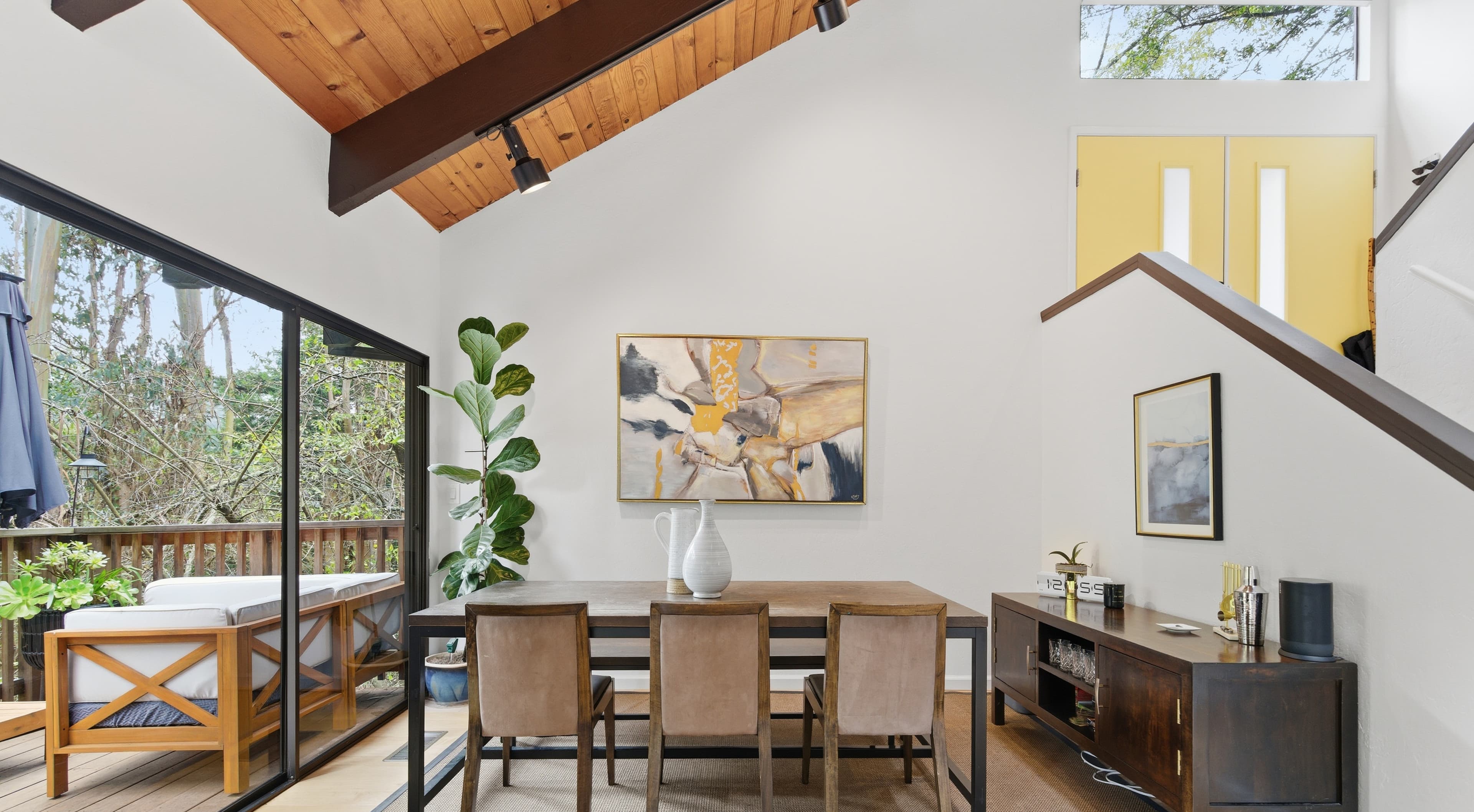 Open-concept living and dining area with a vaulted wood ceiling and glass doors to a deck