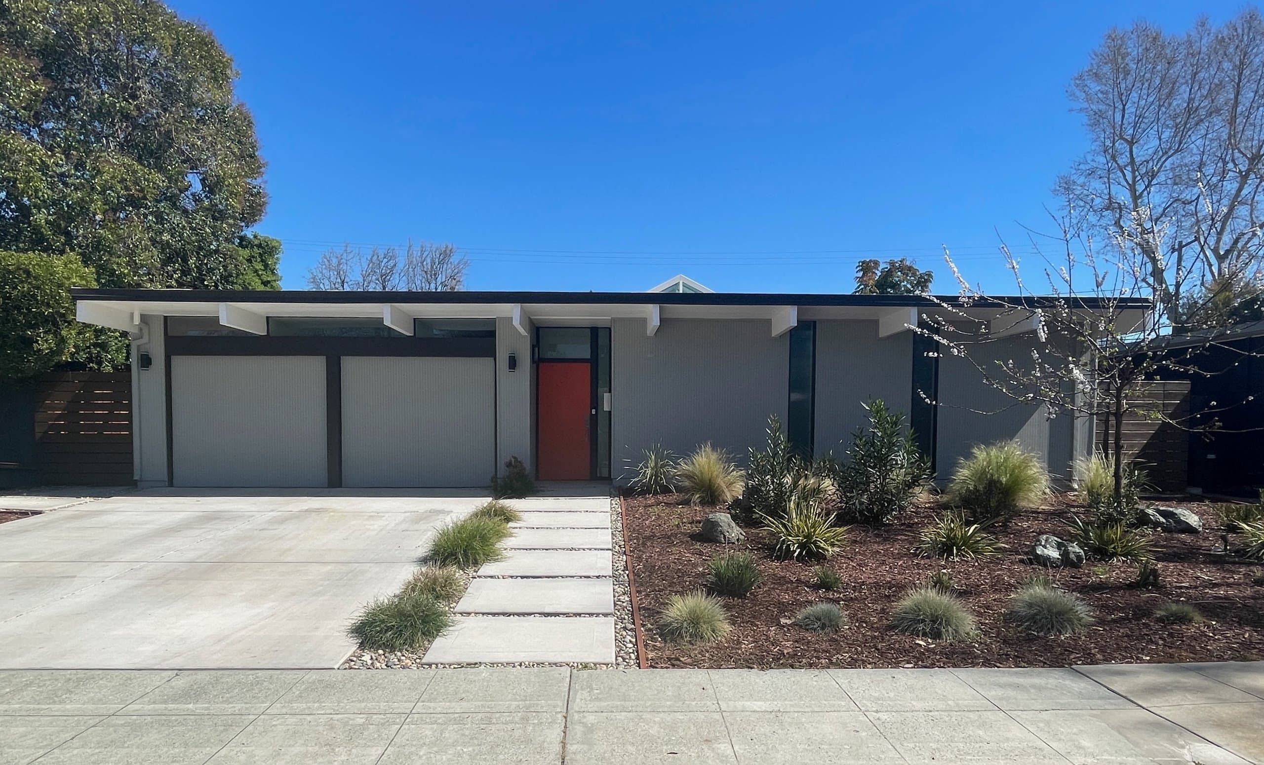 An Eichler's street face: a flat roofline with exposed beam ends, a two-car garage, and a bright orange front door