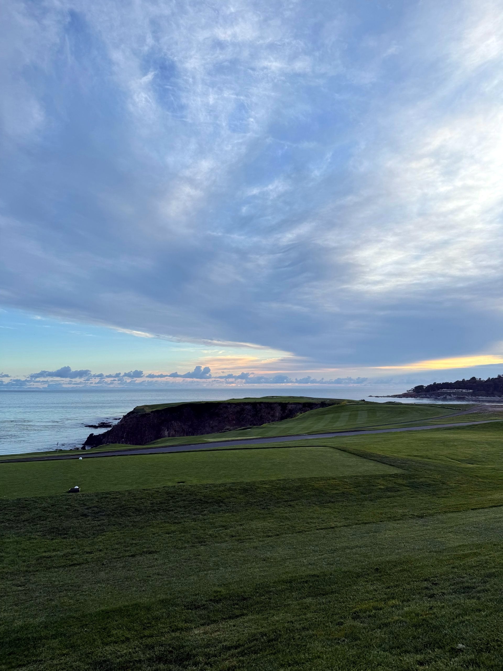 A coastal golf course at sunset, the fairway running out toward the ocean under a sky streaked with clouds